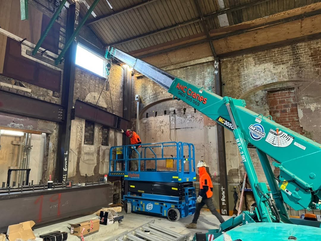 Mini crane assisting with steel work inside an older industrial building